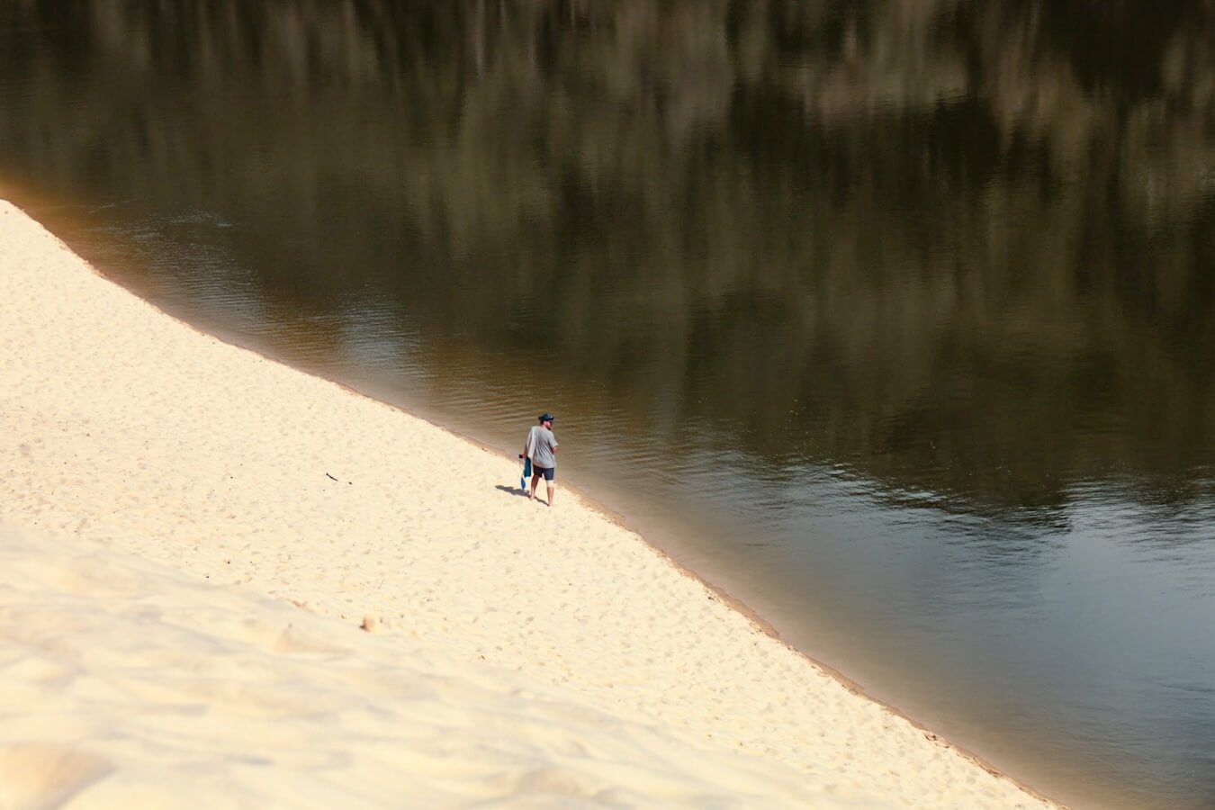 A man stands in the sand dunes, lakeside at Lake Wabby while walking the K'gari Great Walk on Fraser Island.