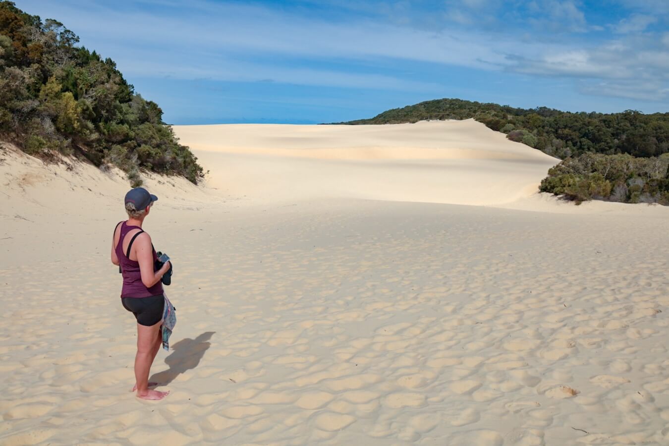 A woman stands in the dunes looking at the Hammerstone sandblow, while walking the K'gari Fraser Island Great Walk
