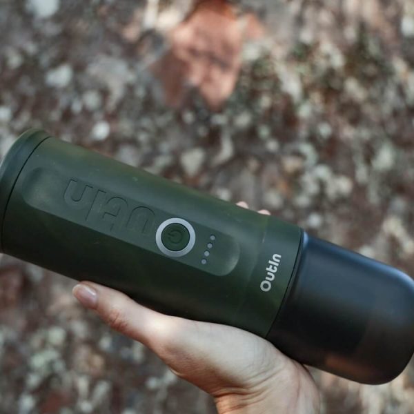 The OutIn automatic portable espresso machine held up in front of a large tree - a camping and travel review.