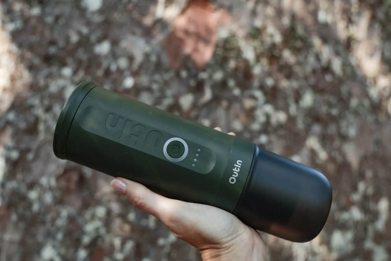 The OutIn automatic portable espresso machine held up for review in front of a large tree.
