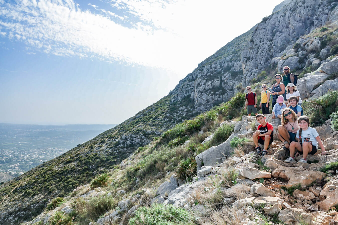 A group of hikers with kids walking on the rocky trail towards the summit of Montgo in Spain