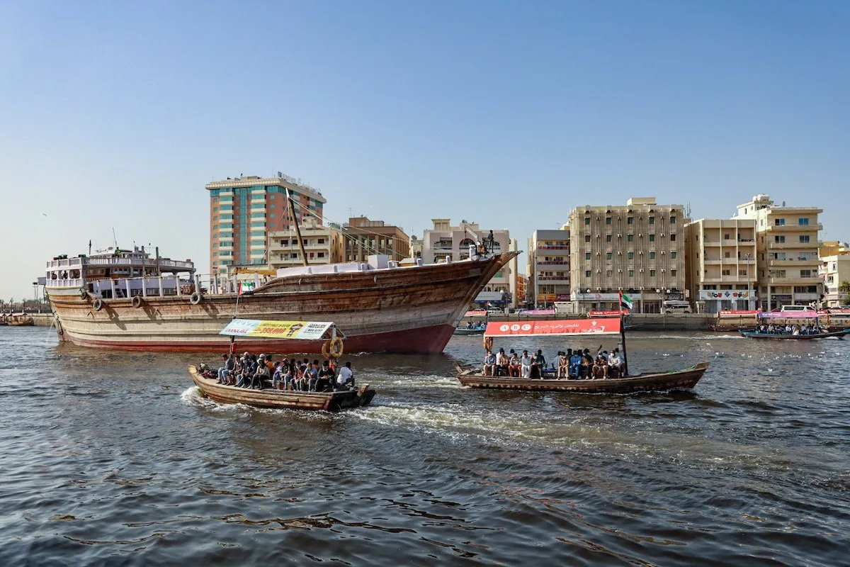 Passengers crossing Dubai Creek on abras with large cargo dhow in behind