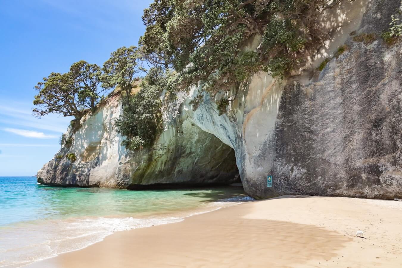 The iconic archway and beach at Cathedral Cove with signs to beware of falling rocks.