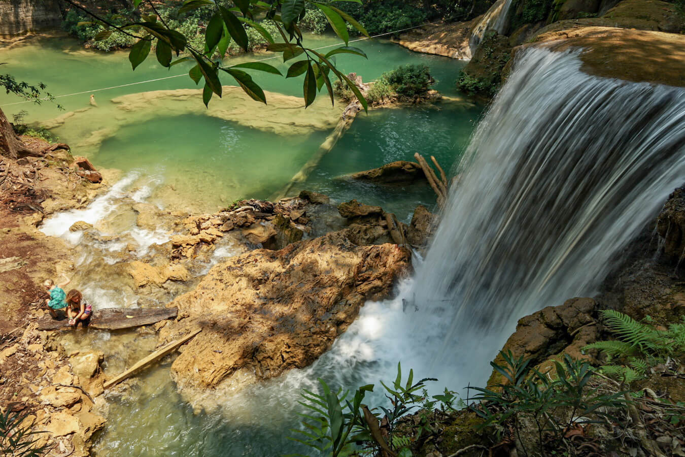 Two young girls sitting at the base of a water fall at Roberto Barrios in Palenque, Mexico.