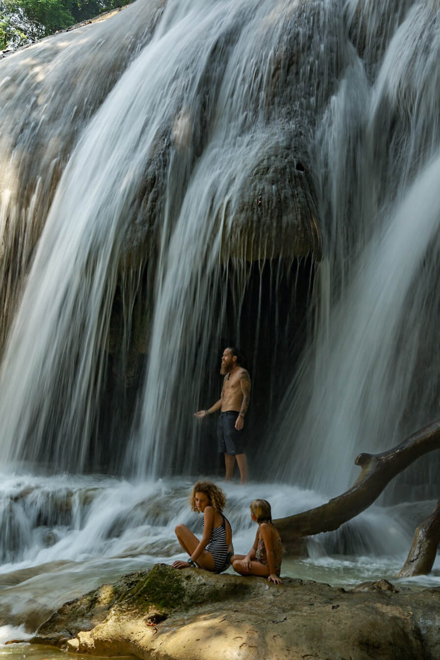 A father standing under a waterfall with his twp daughters looking on, at Roberto Barrios, Palenque, Mexico.