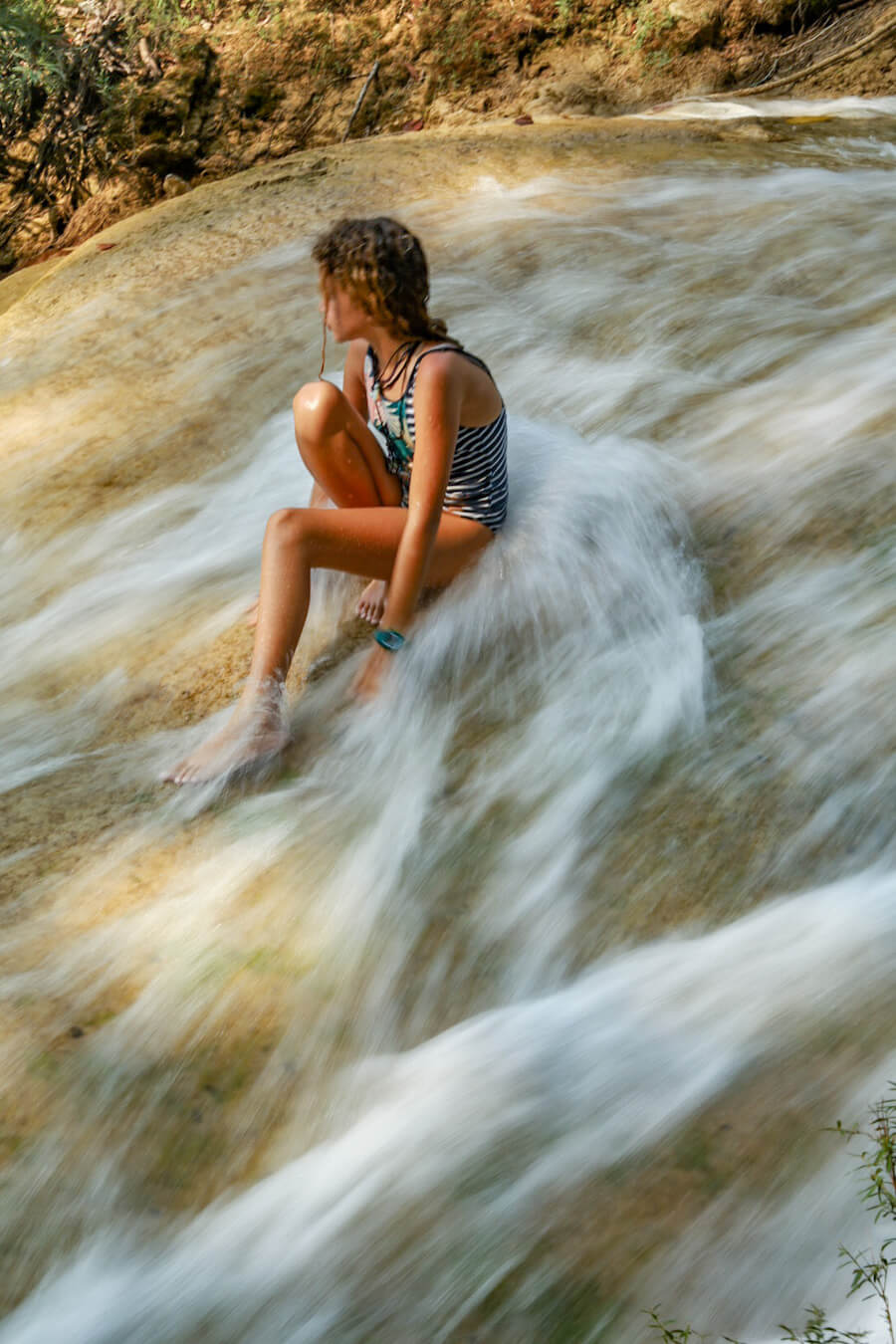 A young girl sitting on a waterfall at Roberto Barrios in Palenque, Mexico.