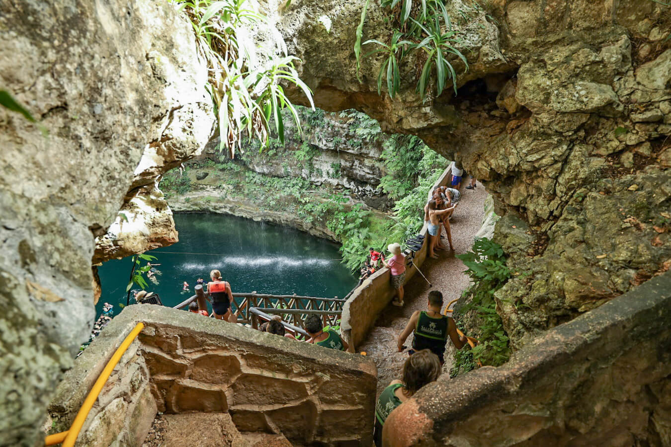 Tourists wearing life jackets walk through the Saamal Cenote entrance down to staircase towards the water.