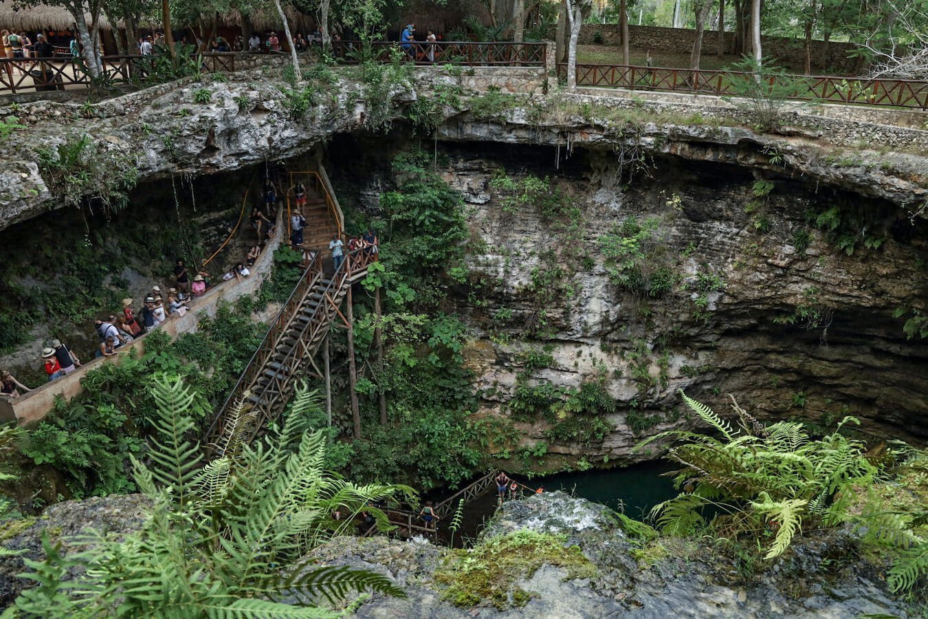 Views of tourists admiring the Saamal cenote and the staircase down towards the cenote water.