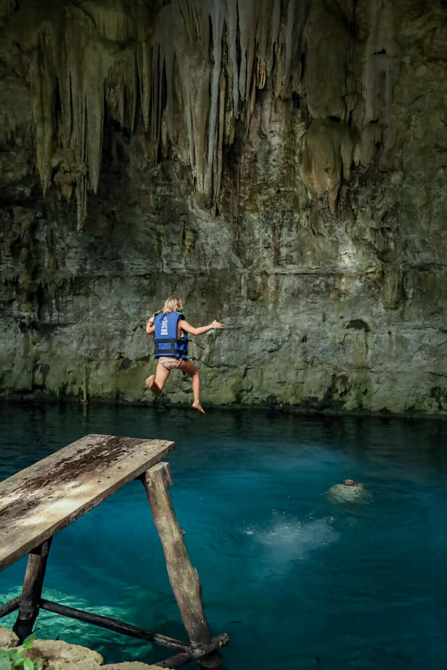 A young child wearing a life jacket leaps into the blue water of Sac Aua cenote - one of the best cenotes near   Valladolid in the Yucatan.