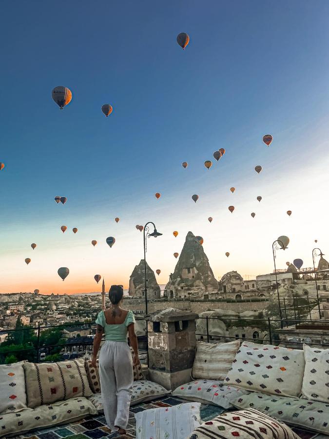 A woman stands on a rooftop terrace in Cappadocia admiring the view of hot air balloons.