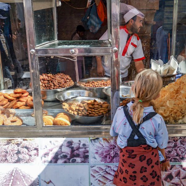 Young girl stands in front of a street food stall in Essaouira with fried tasty treats.