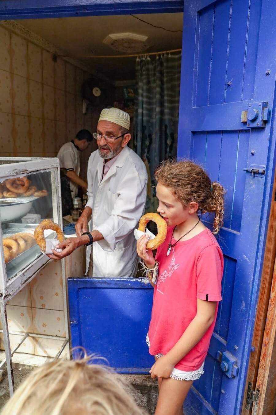 A child eats a donut outside a small road side street food kitchen in Essaouira medina