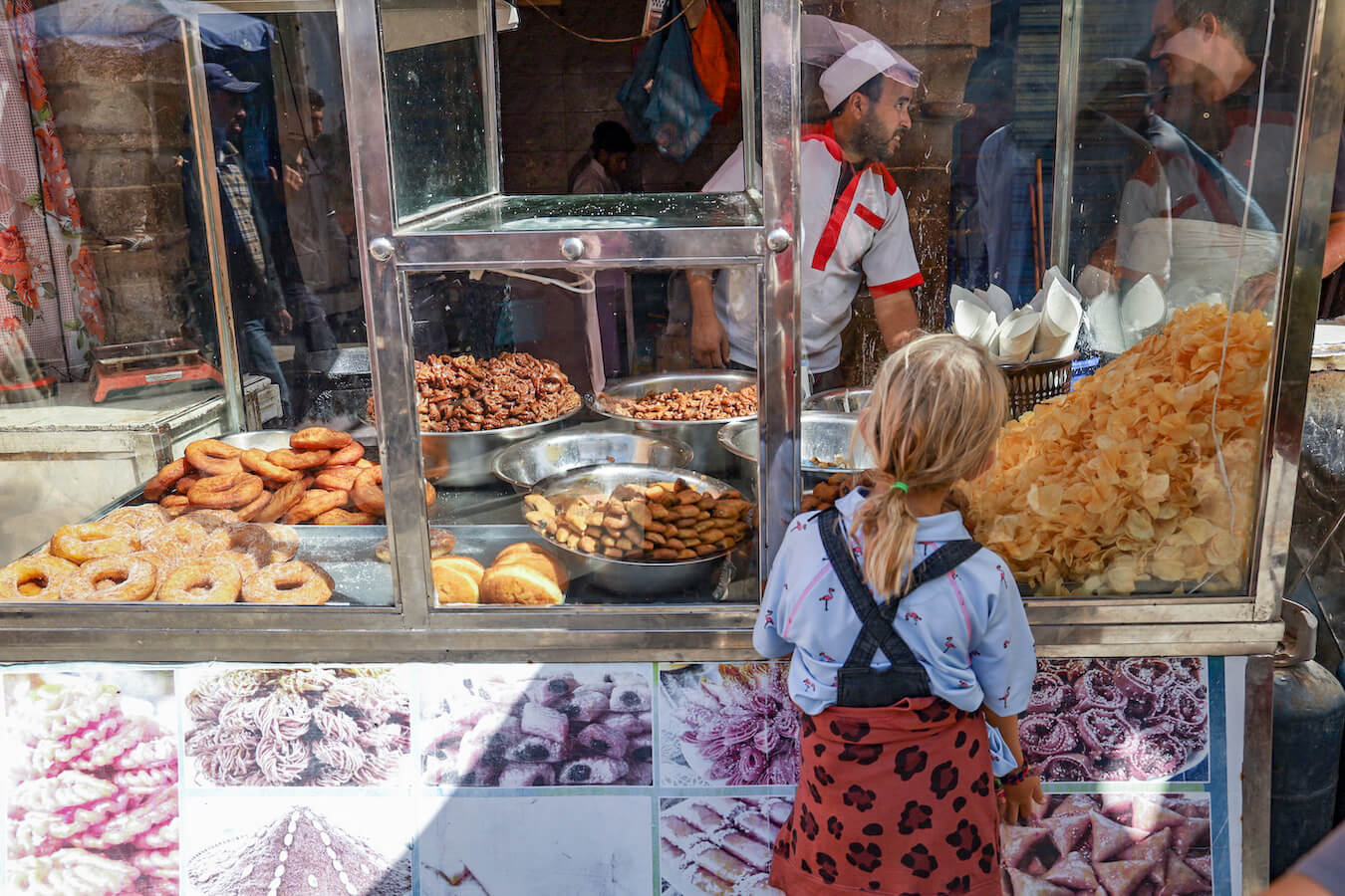 Young girl stands in front of a street food stall in Essaouira with fried tasty treats.