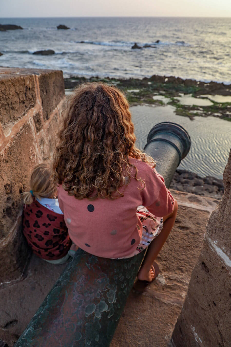 Travel kids look out over rampart walls while sitting on a cannon.