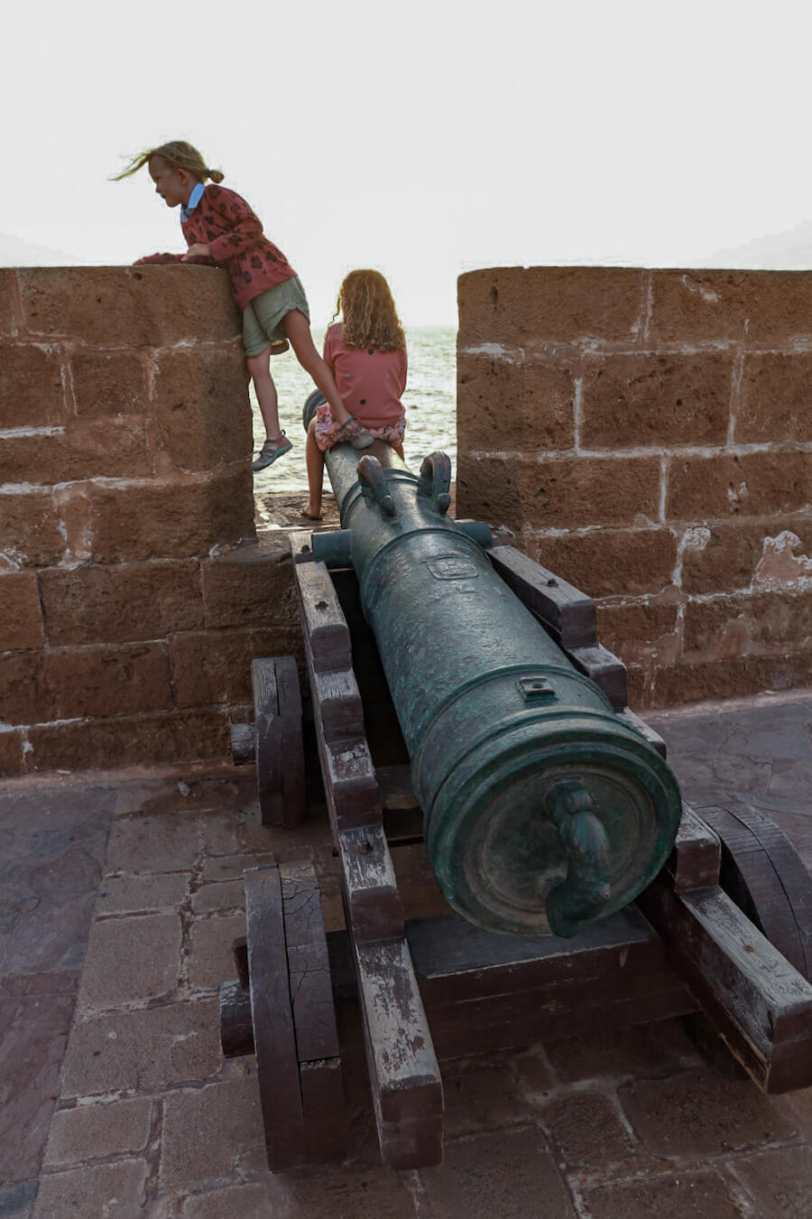 Children sit on cannons on the ramparts in Essaouira, Morocco