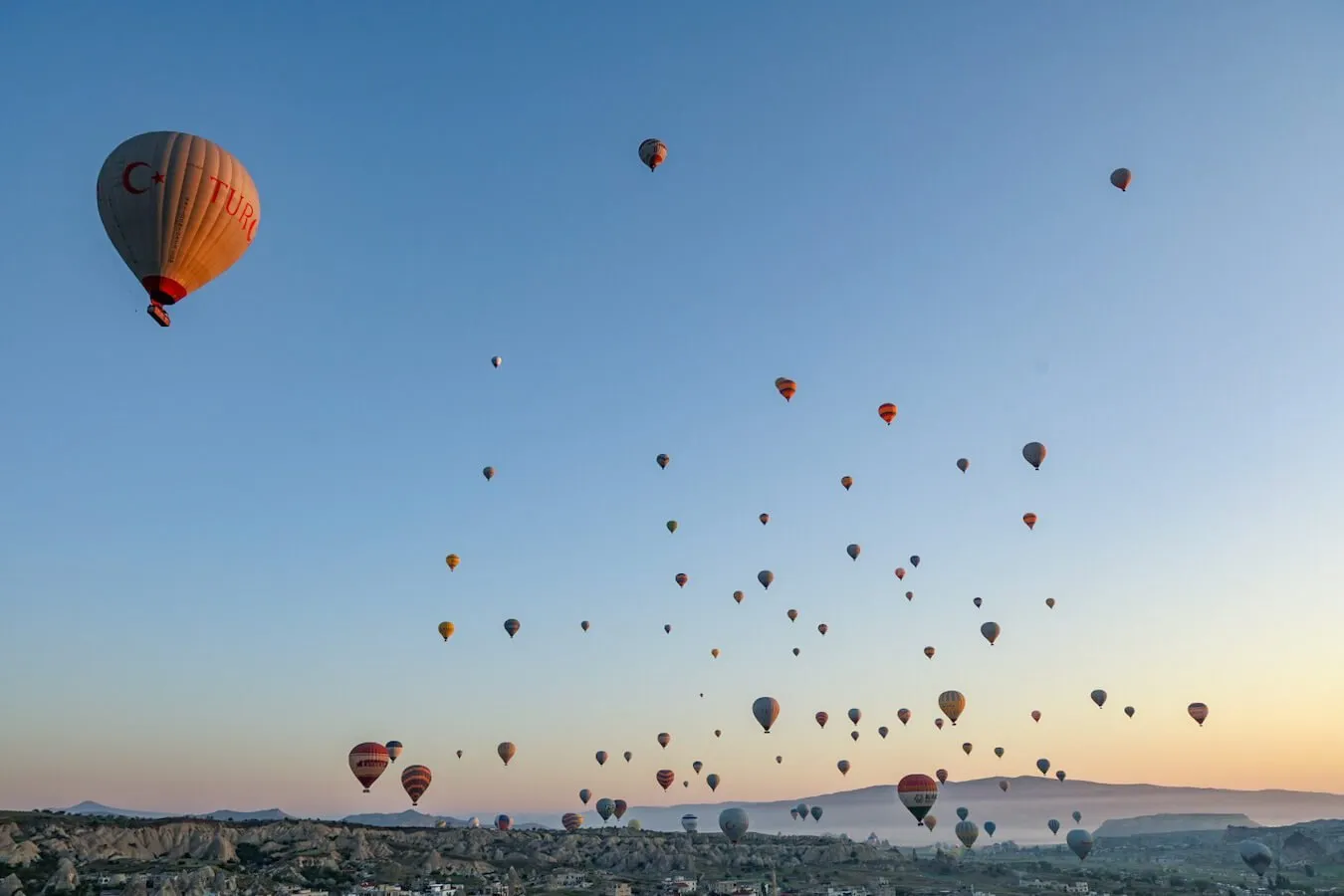 Hot air balloons fill the sky over Cappadocia at sunrise.