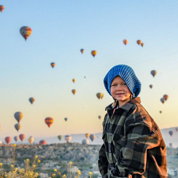 Young child stands at sunrise with hot air balloons in the background - the magical backdrop of Cappadocia