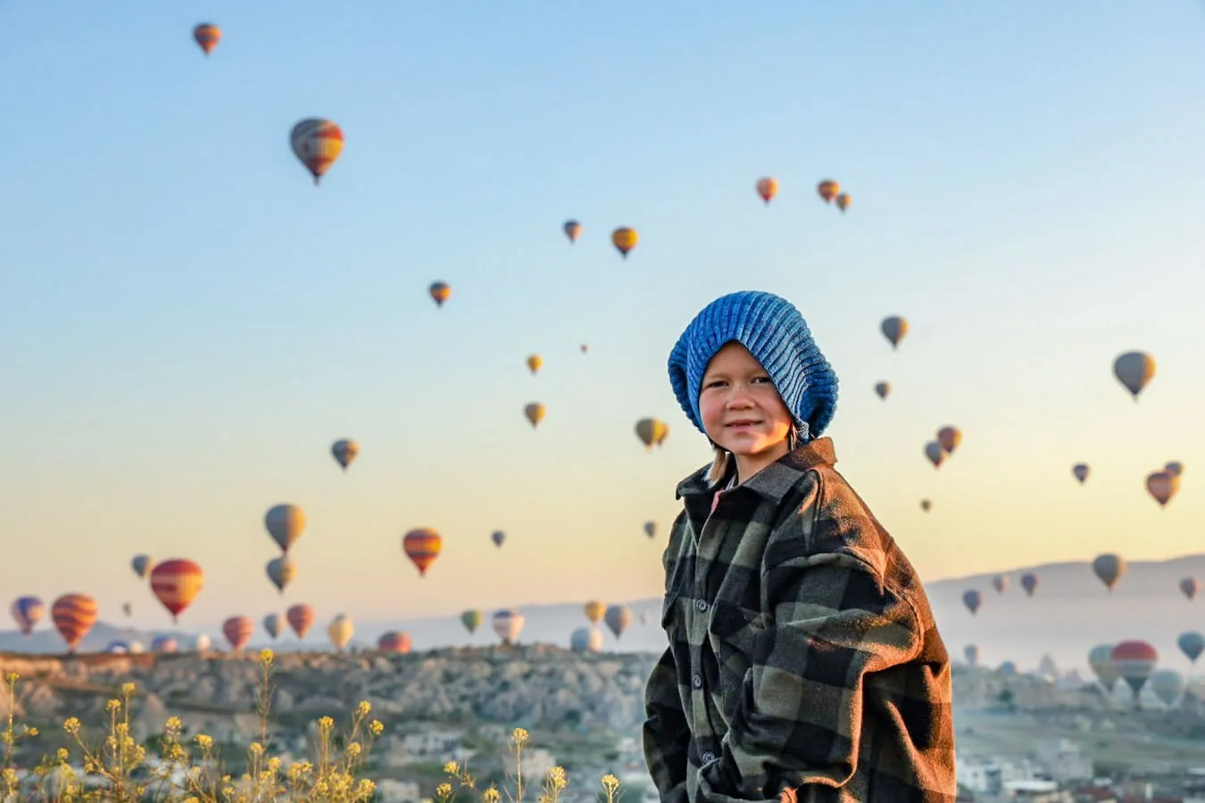 Young child stands at sunrise with hot air balloons in the background - the magical backdrop of Cappadocia 