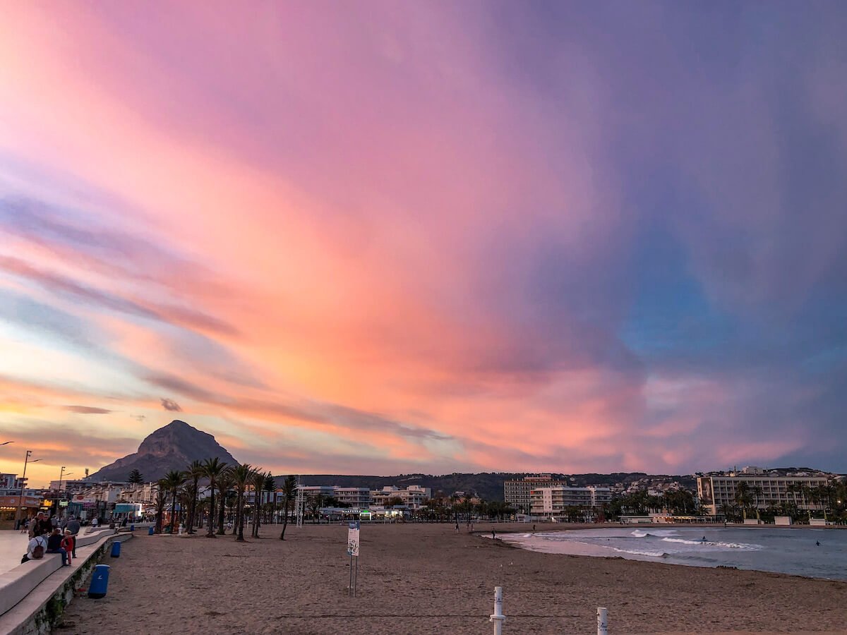 The sun sets over the Arenal beach and promenade in Javea, with Montgo Massif in the background