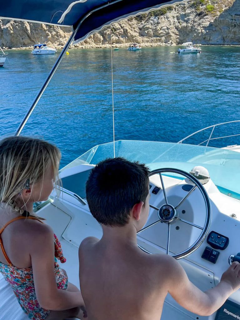 Kids pretend to drive a boat while on a tour in the Mediterranean.