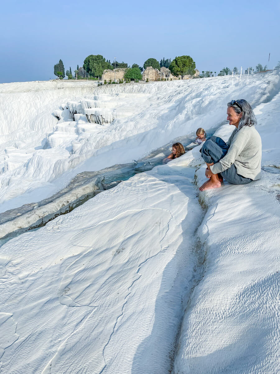 Mother looks out over the white travertine terraces in Pamukkale while her children swim in the warm thermal waters in Spring. Things to do in Pamukkale.