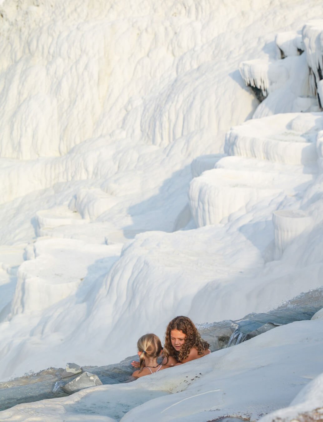 Two children enjoy swimming in the warm thermal waters overlooking the travertine terraces of Pamukkale