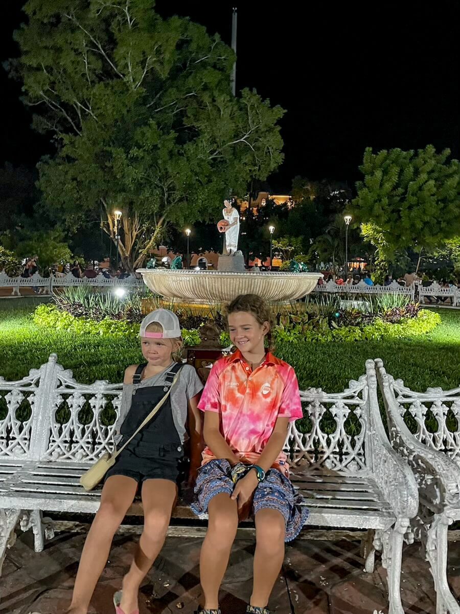 Two kids sit in front of the fountain at night in Parque Principal Francisco Cantón Rosado (the Zocalo) in Valladolid 
