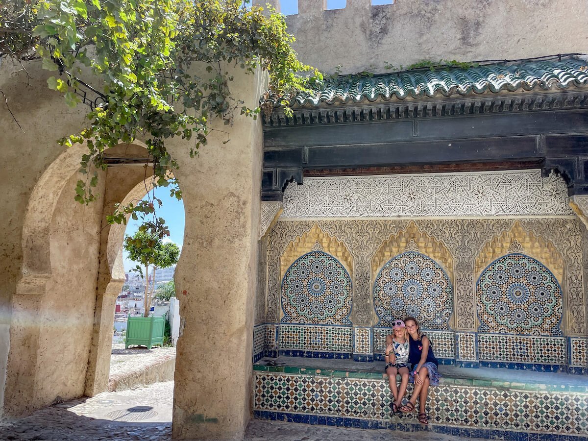 Two kids sit in front of an elaborate wall in Tangier, Morocco. Exploring the streets of the kasbah is just one of the top things to do in Tangier on a 3 day itinerary.