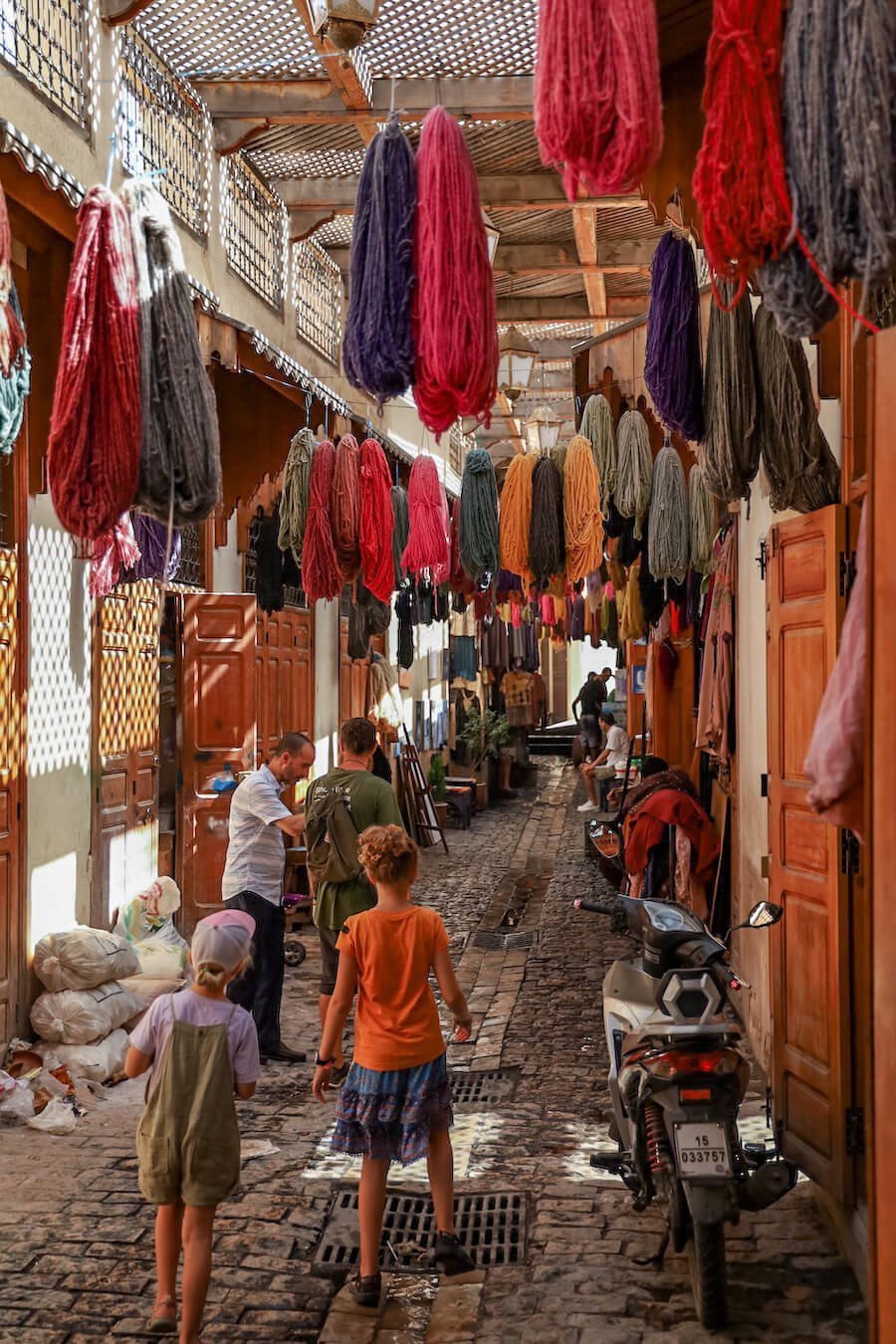 A family walking on a tour through the Fes el-Bali Medina surrounding by dyed yarns of wool.