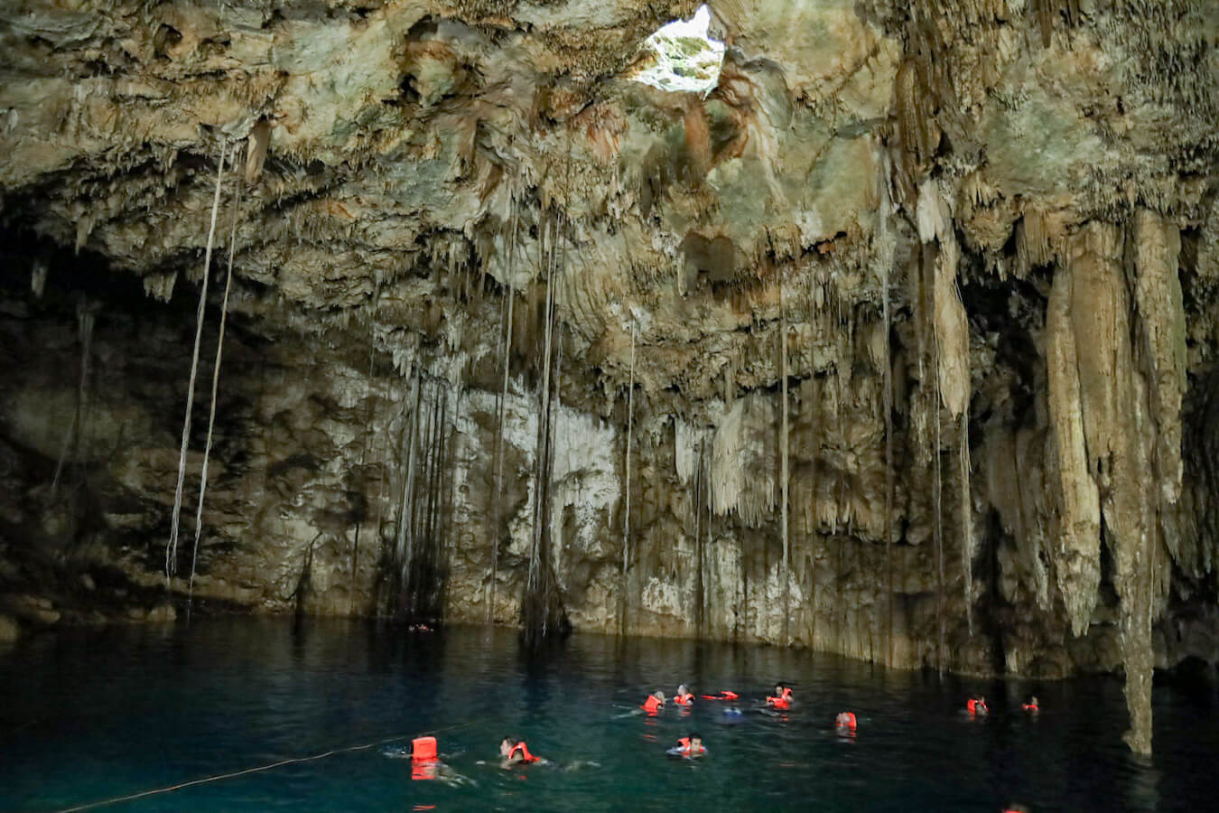 Swimmers float with life jackets under beautiful stalactites in the Xkeken Cenote - the Dzitnup cenotes in Valladolid