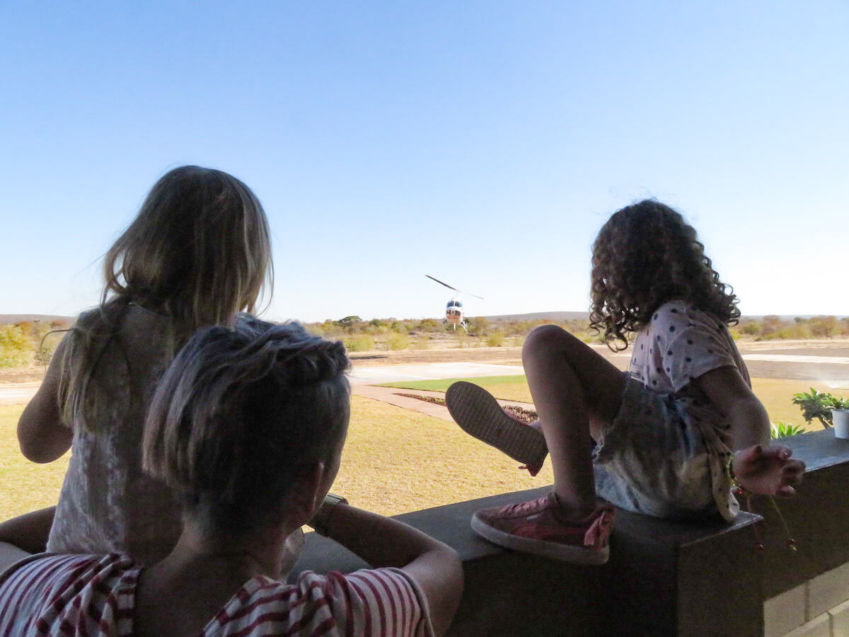 A mother and her two daughters, watch a helicopter come into land, following a tour of the Victoria Falls