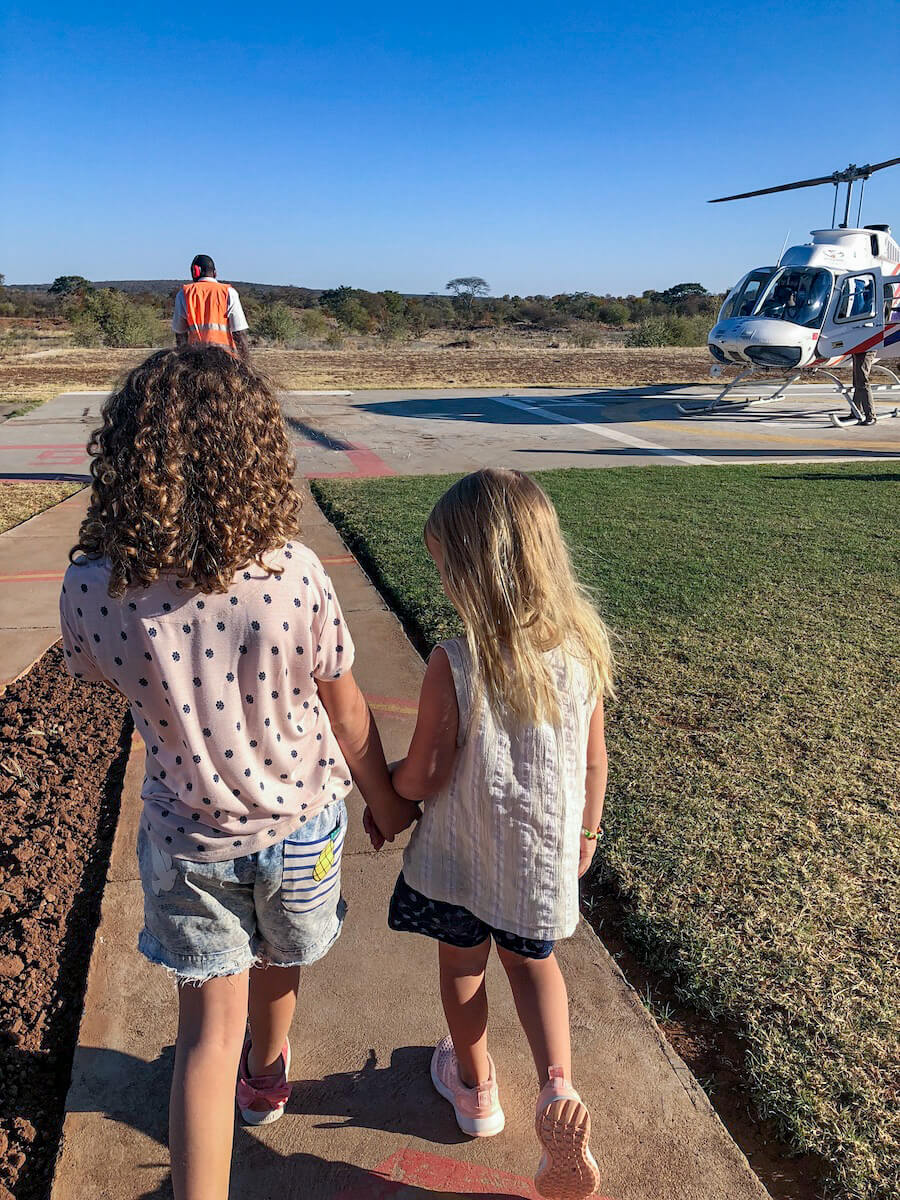 Two kids on holiday in Zimbabwe, walk towards a helicopter for their tour and chopper ride over the Victoria Falls.