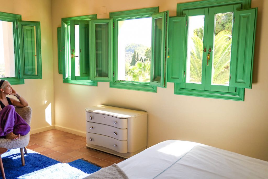 A woman on a weekend getaway looks out the green shuttered windows at Villa Riu Blanc in Costa Blanca in Spain