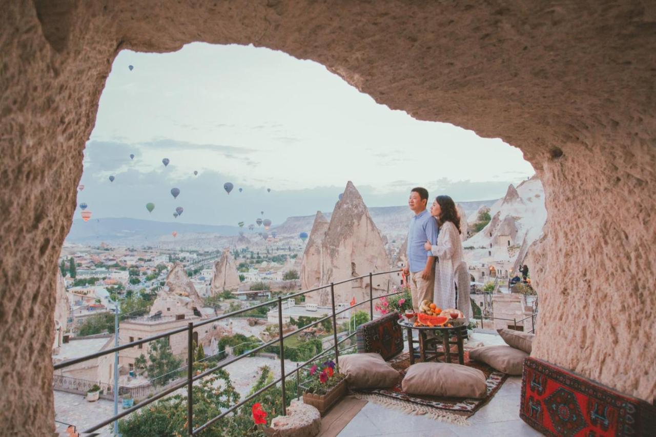 A couple stand on the terrace at Village Cave House Hotel in Cappadocia with views of fairy chimneys and hot air balloons.