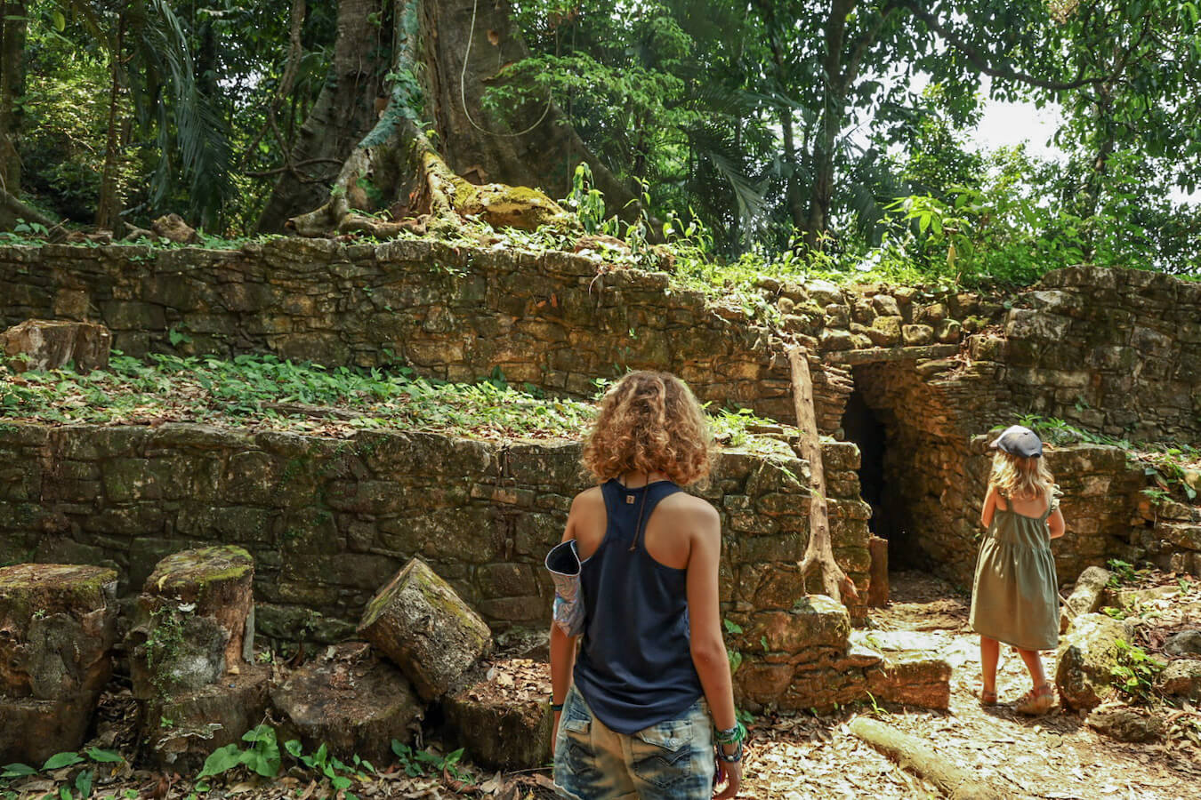 Two young girls walking towards a dark opening inside the ruins of Complexes I & II at Palenque ruins.