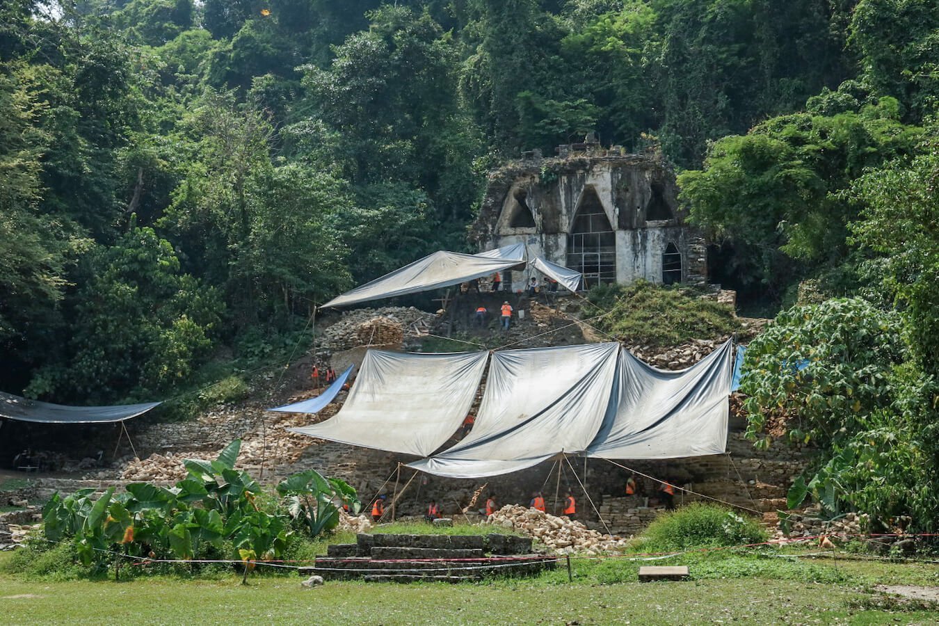 People working under tarpaulins working on the steps and base structure of the Temple of the Foliated Cross at Palenque.