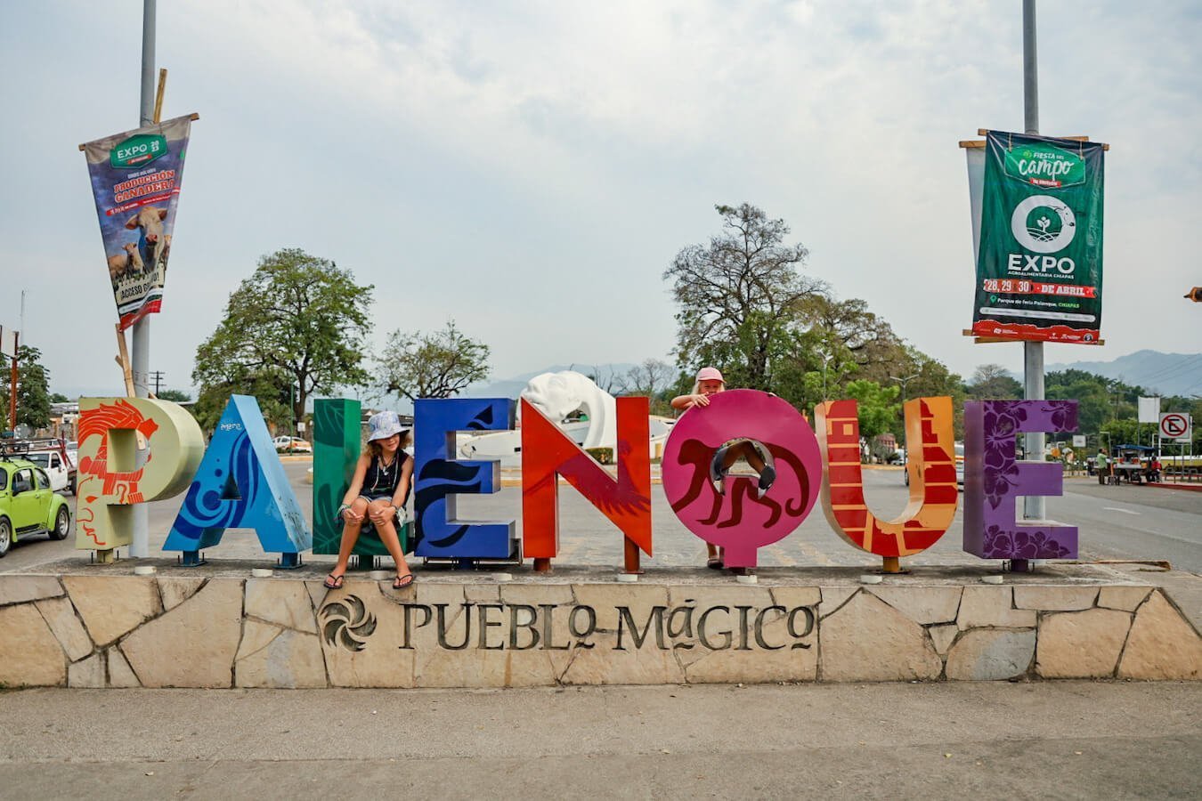 Two young girls sitting on the Palenque, Pueblo Magico sign. 
