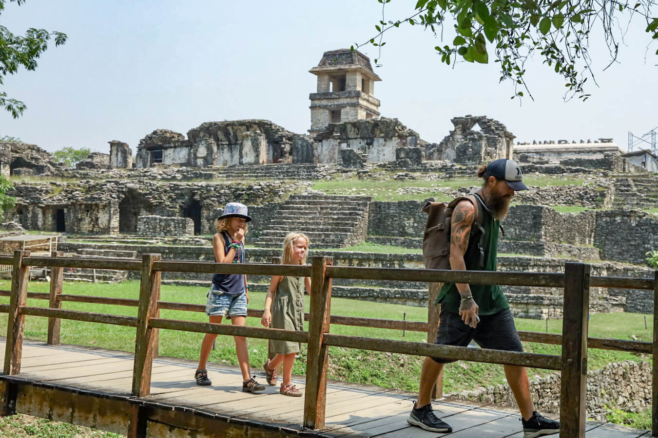 Farther and his two daughters walking over a bridge, with Palenques Palace behind them.