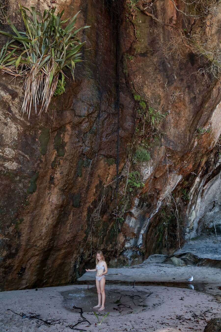 A child stands under the waterfall at the southern end of the beach at Cathedral Cove
