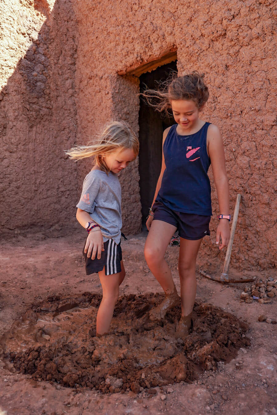 Two girls make mud with their feet, in preparation to make mud bricks in Morocco.