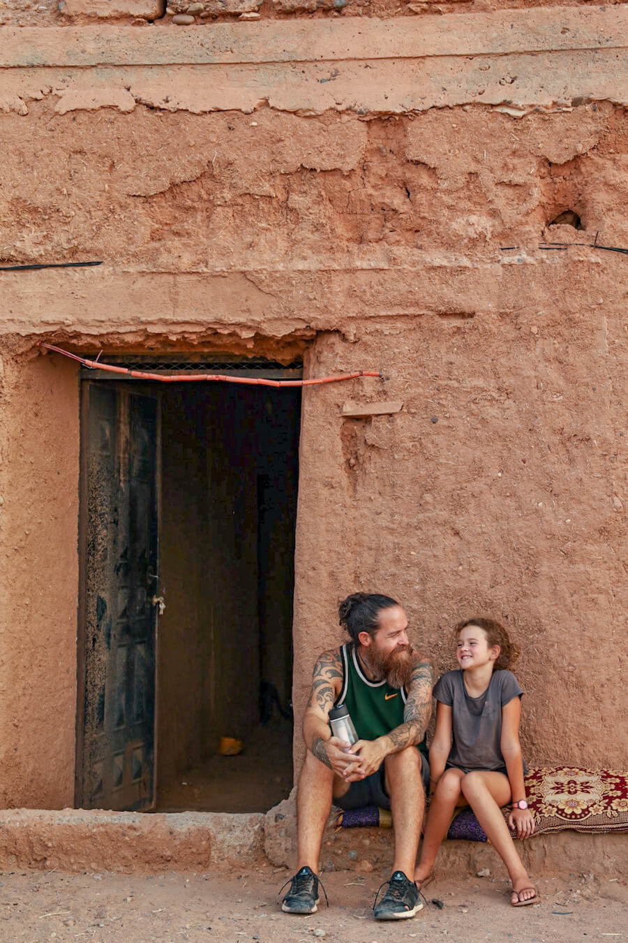 A father and daughter sit outside a mud brick house on a work exchange program in Morocco