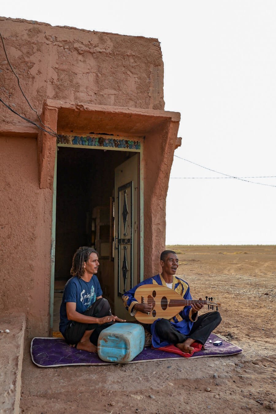 Two local Berbers playing music outside their mud brick home in the Sahara, Morocco.