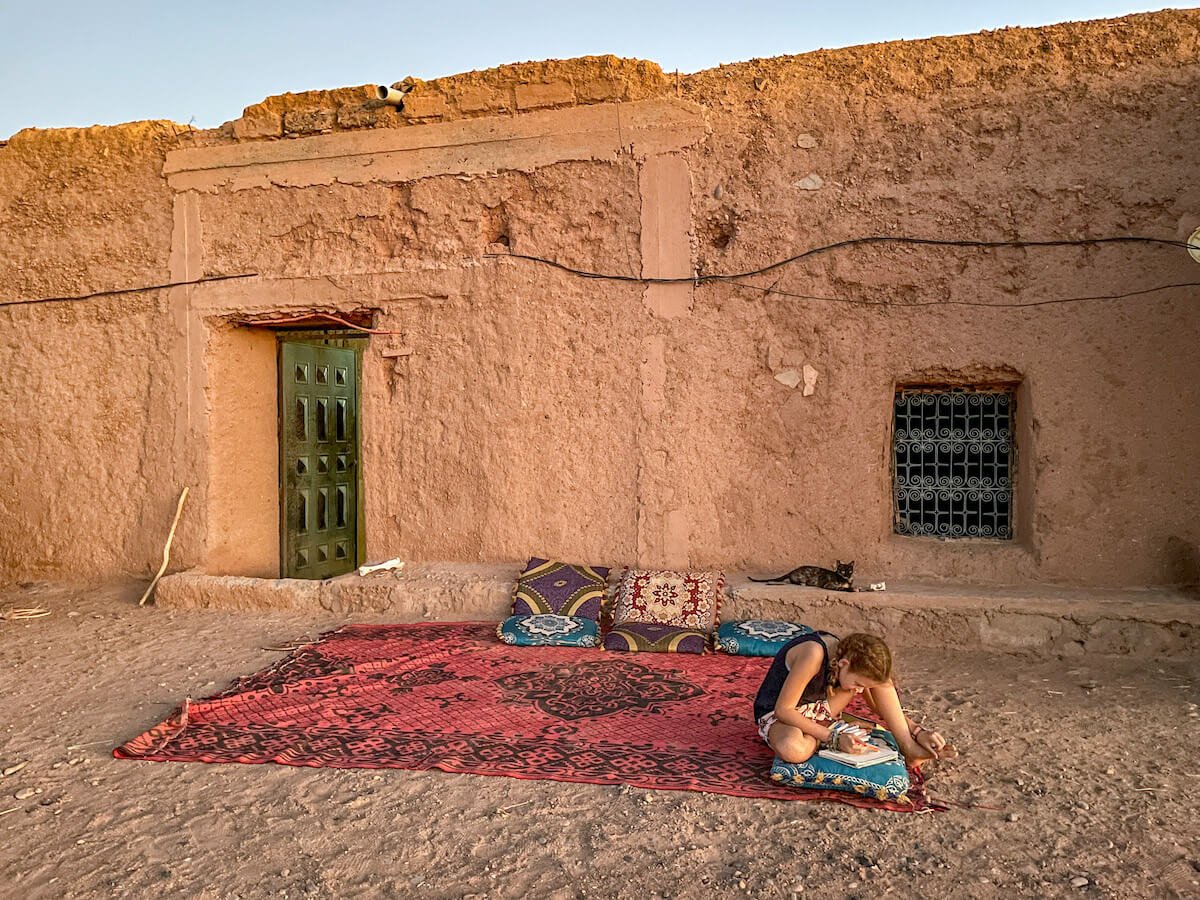 Young girl doing school work outside a mud brick house in Morocco, while on a family work exchange. 