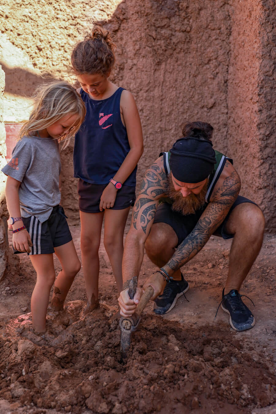 A father and his two daughters preparing mud for the mud brick house they are working on.