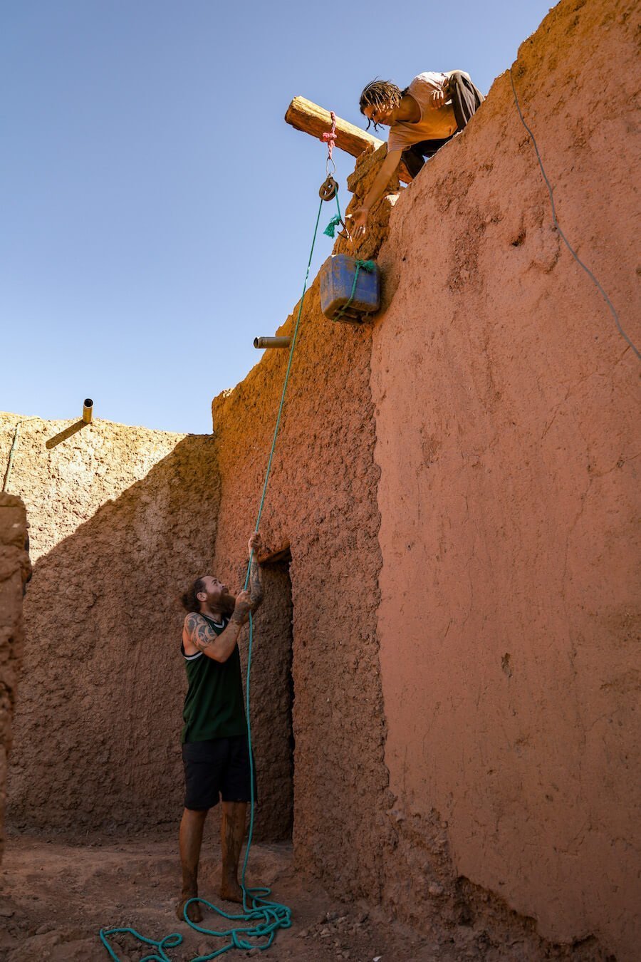 Men on a volunteer and work exchange program in Morocco repair a mud brick house.