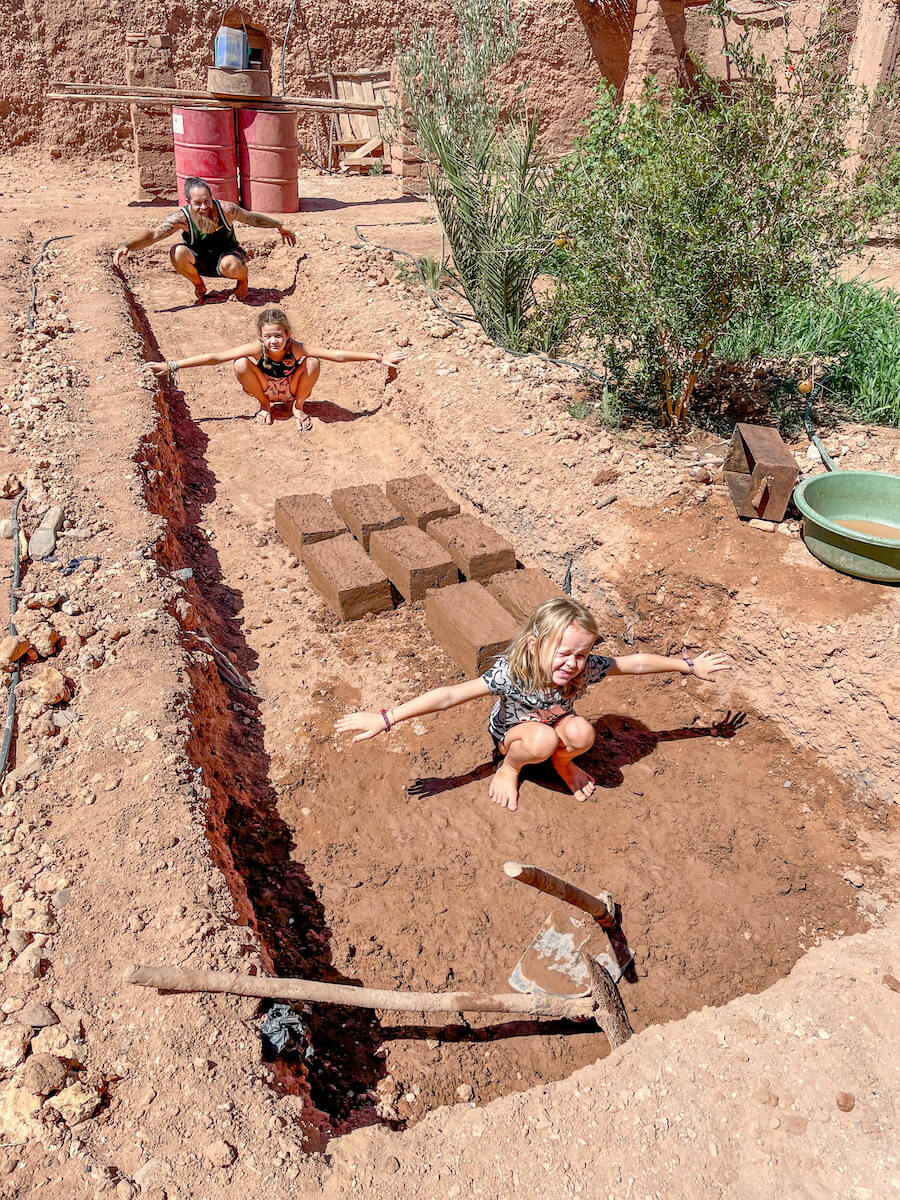 A father and his two daughters sitting inside the site excavated to make mud bricks and plaster during their family work exchange in Morocco.