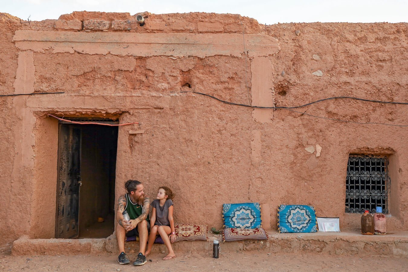 Father and daughter sitting outside their hosts mud brick home while on a work exchange in Morocco.