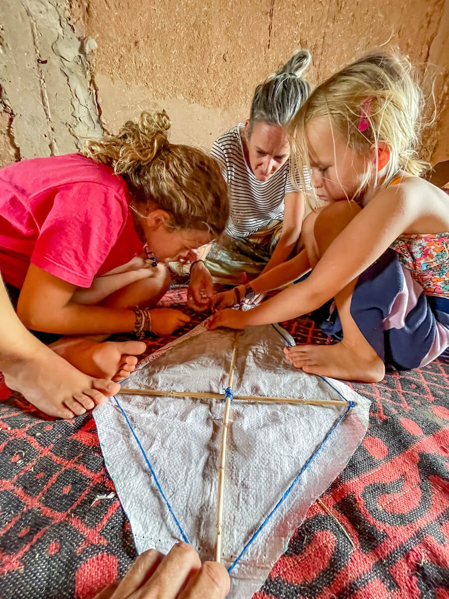 A mother and her two daughters sewing a home made kite together while on a work exchange in Morocco.