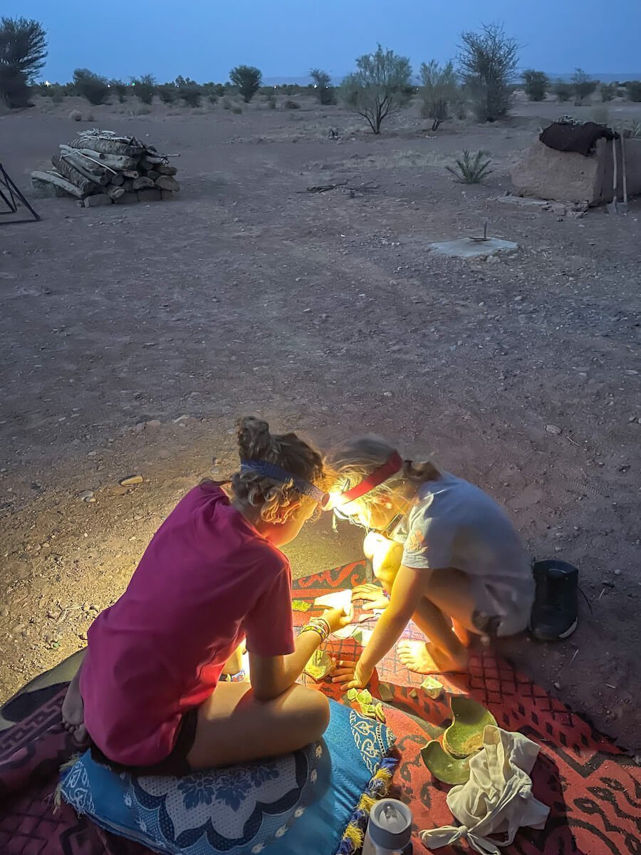 Two girls outside in the evening working by head torch assembling broken pottery.