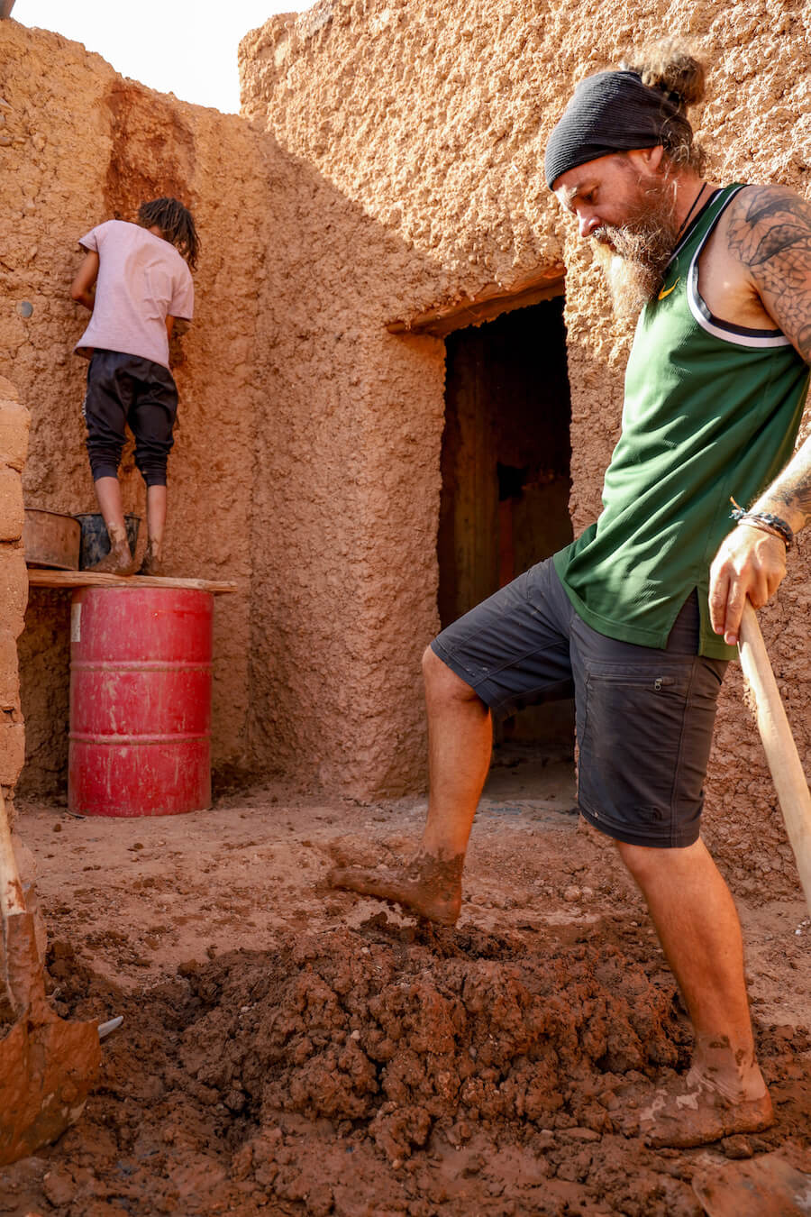 One man preparing mud with his feet and another applying mud to a mud brick house while on a work exchange in Morocco.